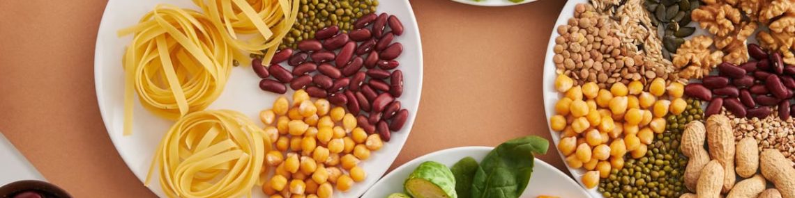 A vibrant mix of legumes, vegetables, nuts, and pasta arranged on white plates showcasing a balanced, healthy diet.